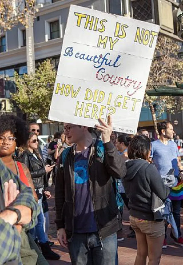 Guy holding sign saying "This is not my beautiful country, how did I get here?