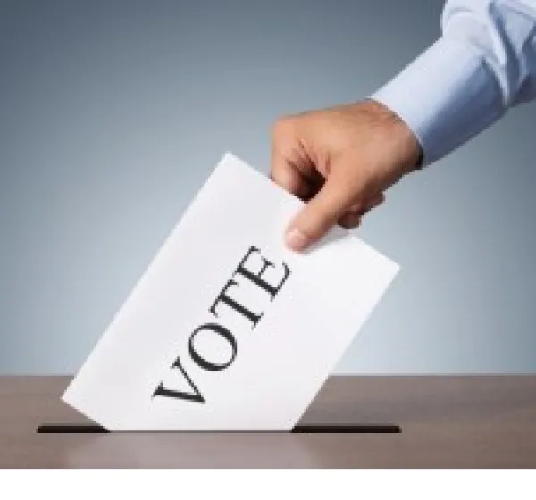 Man's hand putting a paper with the word VOTE on it into a slot in a box