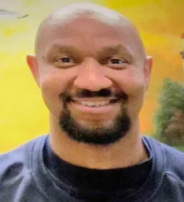 Bald black man with dark mustache and goatee, wearing blue shirt smiling