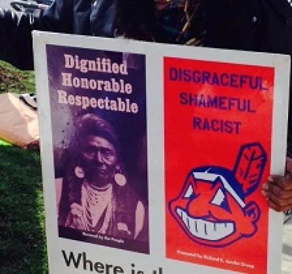 Poster with photo of Native American on left side and big cartoony smily Indian face that is Chief Wahoo the mascot of the Cleveland Indians