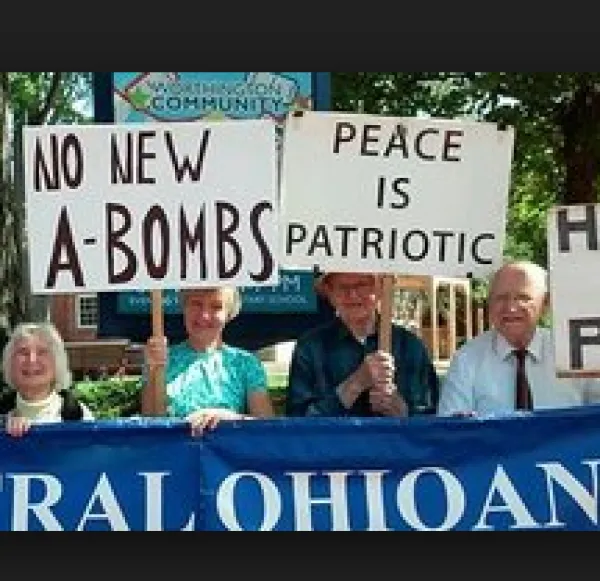 People marching outside with trees in background carrying signs, No New A-Bombs, Peace is Patriotic