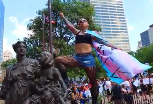 Woman posing on statue wearing trans flag