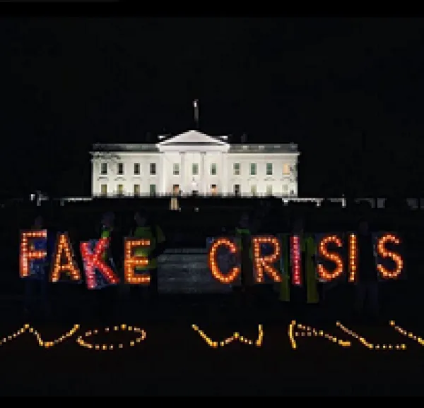 PHoto of white house with neon lights in front against black saying FAKE CRISIS NO WALL