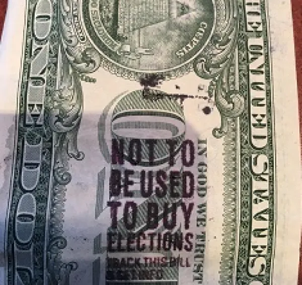 A close up of the back of a dollar bill with a stamp on it saying Not to be used to buy elections
