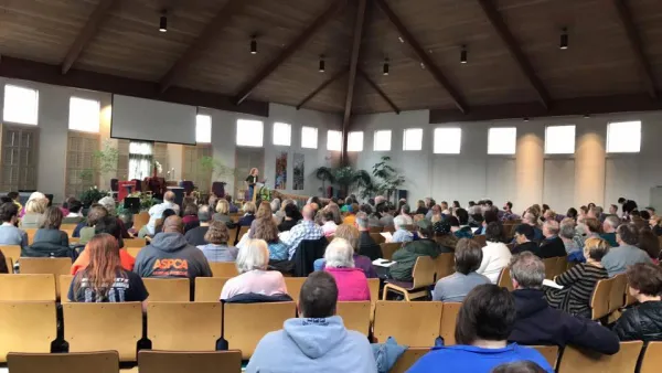 People sitting in chairs in a big hall with their backs to camera