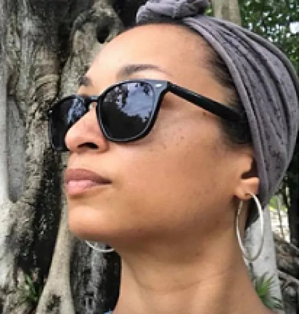 Young black woman with a scarf on her head and sunglasses looking left in front of a tree