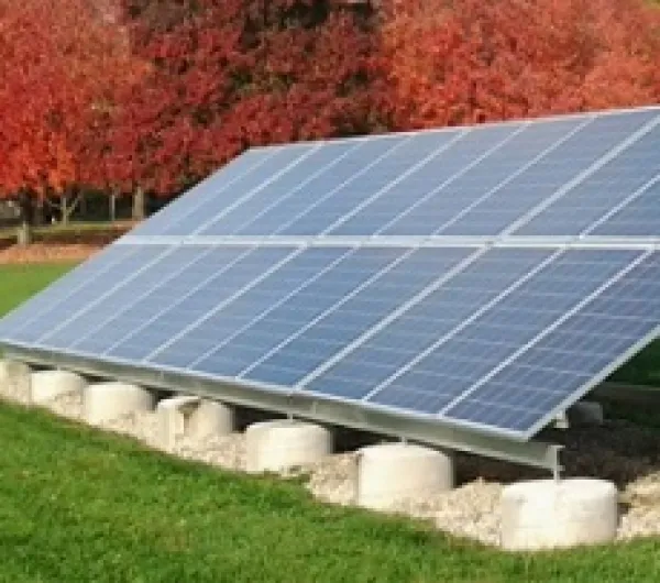 Big silver solar panel on ground sideways aimed at sky with red leaved trees in the background