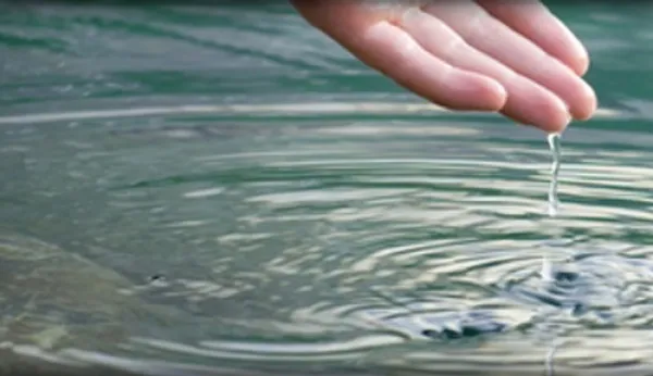 Person's hand above water with drops dripping off