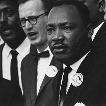 Black man in foreground, Martin Luther King Jr. surrounded by other men 