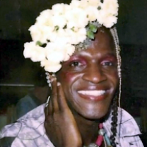 Photo of black woman smiling with her hand by her cheek and lots of white flowers in her hair