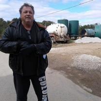 White man in winter coat standing in front of metal tanks and a truck