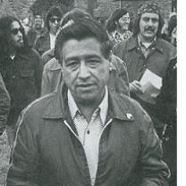 Black and white photo of Latino man wearing a jacket outside in front of a lot of other people