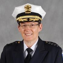 White woman in wire-rimmed glasses smiling in a pose with a police hat and uniform on