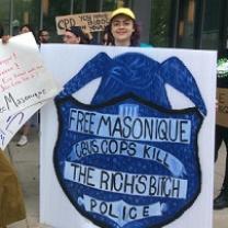 Woman holding a huge sign with a police badge that says Free Masonique Cbus Cops Kill 
