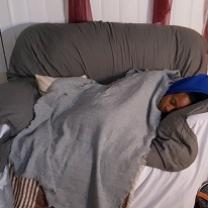 Young black woman asleep under huge blanket on a gray loveseat