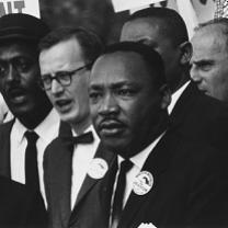 Black man in foreground, Martin Luther King Jr. surrounded by other men with sign above saying Now