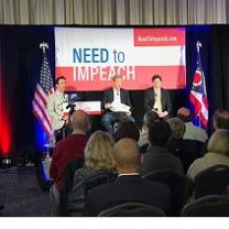 Red and white banner in the back between flags saying  Need to Impeach, three white men sitting facing the audience