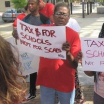 Black woman outside at rally holding a sign that says Tax $ for Schools Not for Scabs