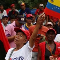 People of color outside at a rally one woman in front waving a red, blue and yellow striped flag