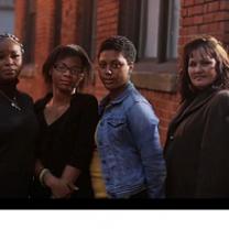 Three black women and a white woman standing outside looking very serious