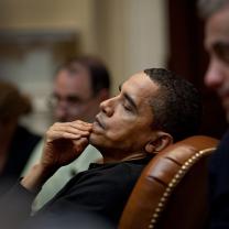 Obama leaning back in leather chair with hand on mouth looking pensive