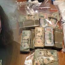 Mug shot of disheveled white guy with long hair next to money and drugs