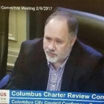 Bald man with gray goatee at a official city meeting