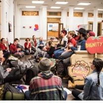 Dozens of kids sitting around an office with a tomato sign that says Dignity