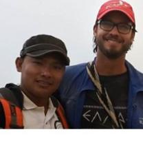 Young looking boy of color with a baseball cap next to a white man with beard and mustache and glasses with a baseball cap on smiling