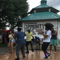 Young black people dancing outside in front of a gazebo with a Columbus Community Pride banner