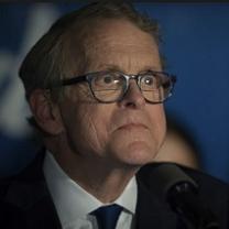 Older white man with glasses looking weird and crazy in a suit at a microphone