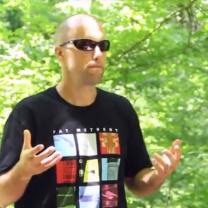Young white man mostly bald holding his hands out in front of him standing in a forest