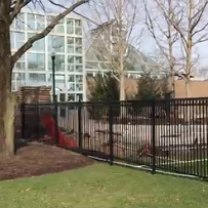 Iron gate with grass and trees on one side and big building with a lot of windows on the other side