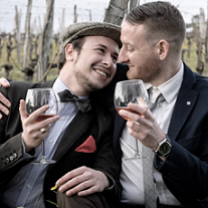 Two white guys one in a beret drinking wine and cuddling outside