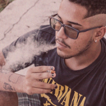 Young black man with glasses blowing smoke out of his mouth with a cigarette in his hand