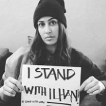 Black and white photo of woman holding small sign saying I Stand with Ilhan