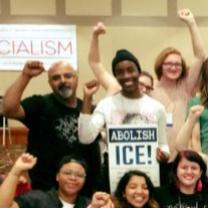 People smiling with fists in the air and a sign that says Socialism and one that says Abolish ICE