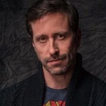 Thin faced man with brown hair and five o clock shadow looking quizzically at the camera
