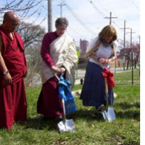 Three people digging into the ground, two wearing Buddhist garb