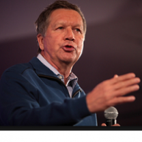 Older white man gesturing as he speaks holding a mic