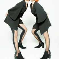 Two women with red hair and black outfits leaning towards each other