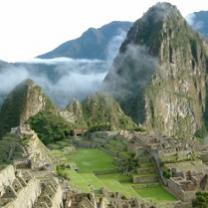 Tall mountain at right against other mountains in the background lower ones toward the left green grass and low clouds