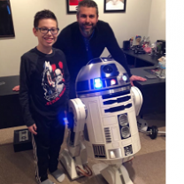 Man and young boy posing next to a robot that has a round top and white round body