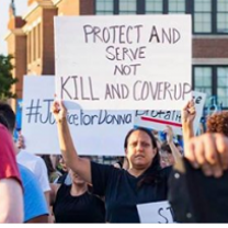 Woman outside holding a sign that says Protect and Serve not Kill and Coverup