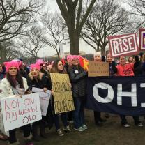 Women outside wearing pink winter hats holding signs and a big banner that says OHIO