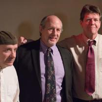 Four middle aged white guys, some in suits, standing together with their arms around each other