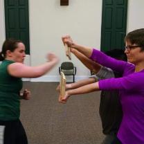 Two women one holding a board and the other one getting ready to karate chop it
