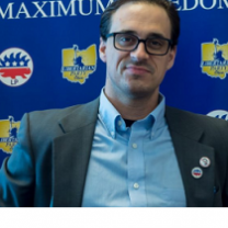 White man with black rimmed glasses in a suit coat