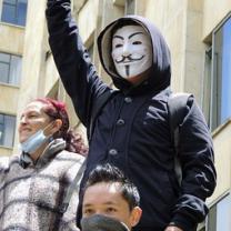 Guy wearing anonymous Guy Fawkes mask with fist in air at protest with others 