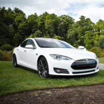 White sports car sitting outside on a green lawn with trees in the background